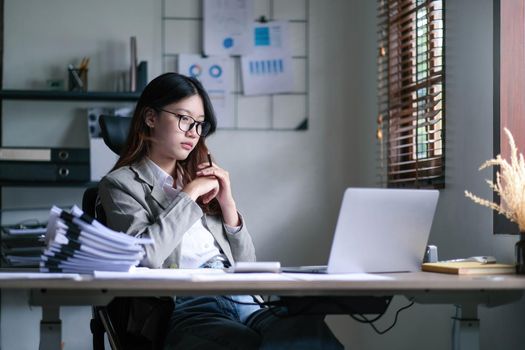 Young Asian woman feeling migraine head strain. Tired, Overworked businesswoman financier while working on laptop computer in office..