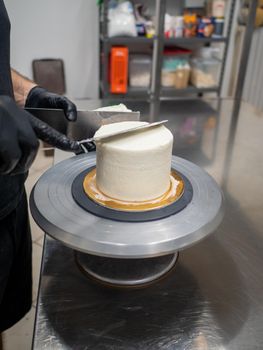 Decorator using spatula and scraper to smooth buttercream on a frosted cake