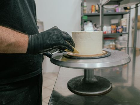 Decorator using spatula and scraper to smooth buttercream on a frosted cake