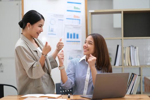 Happy business asian people are keeping arms raised hi five and expressing joyful while standing. achieving goals..