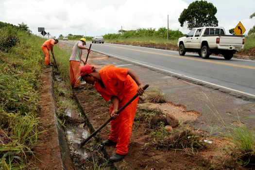 porto seguro, bahia / brazil - jmay 5, 2009: workers are seen cleaning up the water drainage area on the side of the highway BR 367 in the city of Porto Seguro.
