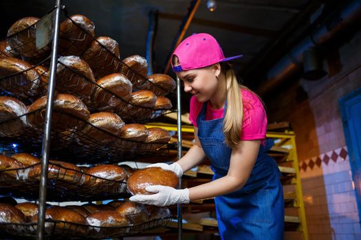 A young girl works in a bakery. She puts bread on a shelf. Woman baker at workplace in a bakery. A professional baker holds bread in his hands. Bread production concept