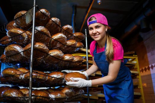 A young girl works in a bakery. She puts bread on a shelf. Woman baker at workplace in a bakery. A professional baker holds bread in his hands. Bread production concept