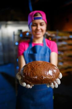 A baker girl takes hot bread in a bakery against the background of shelving with bread. Industrial production of bread. The stage of baking in a bakery