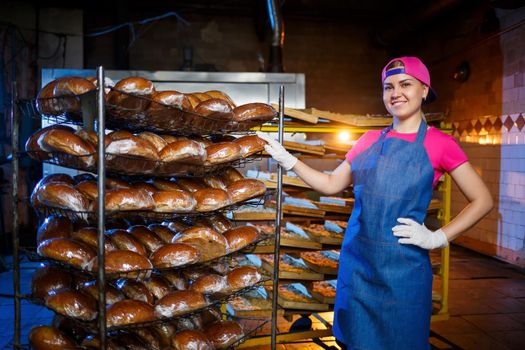 A young girl works in a bakery. She puts bread on a shelf. Woman baker at workplace in a bakery. A professional baker holds bread in his hands. Bread production concept