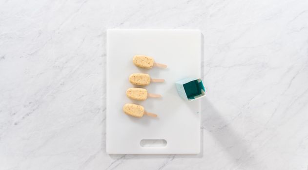 Flat lay. Dipping frozen cakesicles into melted chocolate to prepare mermaid cakesicles.