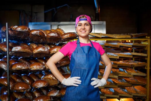 Portrait of a baker girl against the background of shelves with fresh bread in a bakery. Industrial bread production