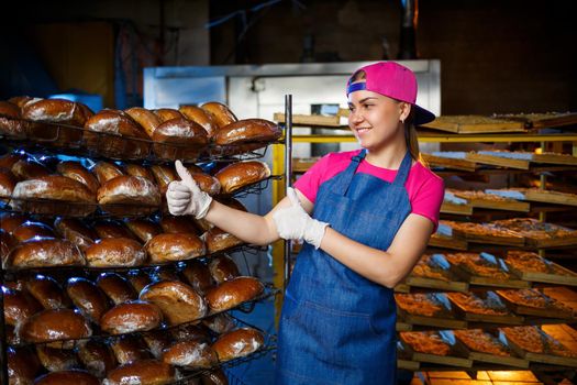 Portrait of a baker girl against the background of shelves with fresh bread in a bakery. Industrial bread production
