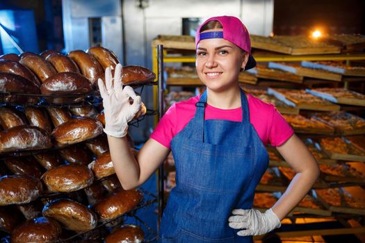 Portrait of a baker girl against the background of shelves with fresh bread in a bakery. Industrial bread production