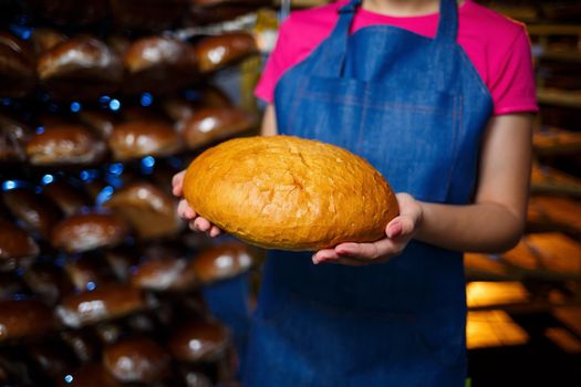 A worker works in a bakery. She puts bread on a shelf. Fresh crispy bread close-up