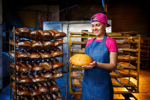 A baker girl takes hot bread in a bakery against the background of shelving with bread. Industrial production of bread. The stage of baking in a bakery