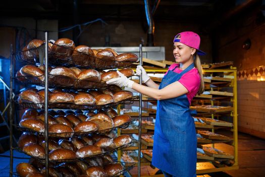 Professional baker - a young pretty woman in a denim apron holds fresh bread in her hands. Bakery products. Bread production