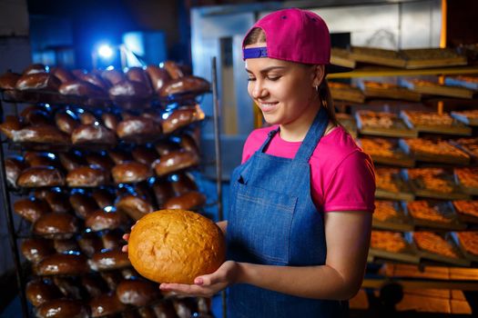 The stage of baking in a bakery. Portrait of a baker girl with bread in her hands against the background of shelving in a bakery. Hands of a baker with bread. Industrial bread production