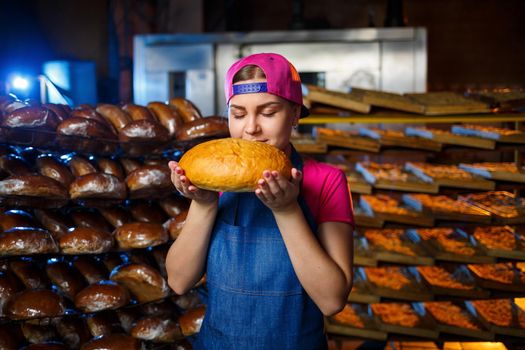 Portrait of a baker girl with bread in her hands on the background of shelves in a bakery. Baker's hands with bread. Industrial production of bread