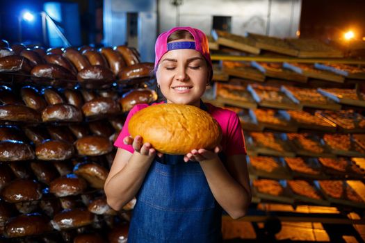 The stage of baking in a bakery. Portrait of a baker girl with bread in her hands against the background of shelving in a bakery. Hands of a baker with bread. Industrial bread production