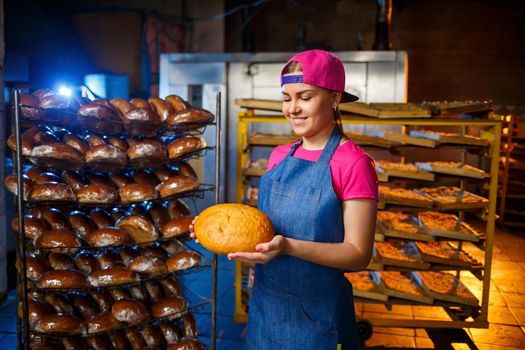 A baker girl takes hot bread in a bakery against the background of shelving with bread. Industrial production of bread. The stage of baking in a bakery