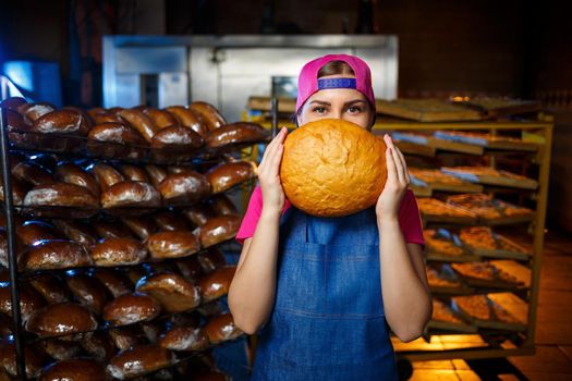 The stage of baking in a bakery. Portrait of a baker girl with bread in her hands against the background of shelving in a bakery. Hands of a baker with bread. Industrial bread production