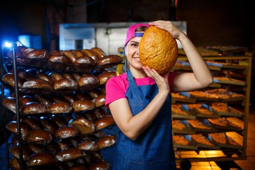 The stage of baking in a bakery. Portrait of a baker girl with bread in her hands against the background of shelving in a bakery. Hands of a baker with bread. Industrial bread production