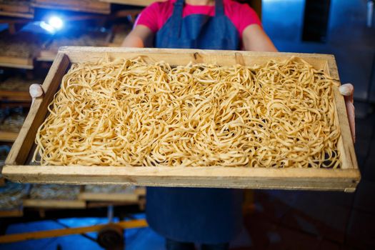 The girl works on the production of spaghetti. Making noodles. Pasta factory. Stage production of pasta. Raw noodles. Worker with a box of pasta.