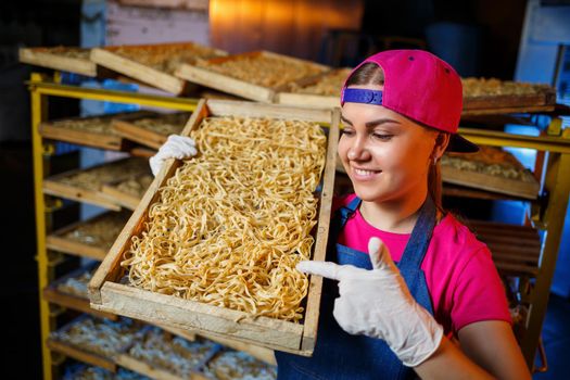 The girl works on the production of spaghetti. Making noodles. Pasta factory. Stage production of pasta. Raw noodles. Worker with a box of pasta.