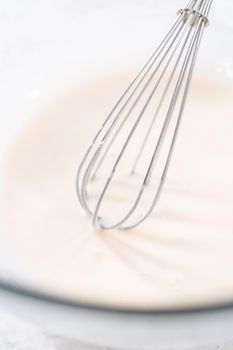 Mixing ingredients in a glass mixing bowl to prepare the white glaze.