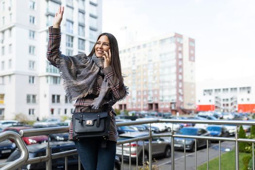 young woman talking on the phone waving her hand to her friend with a smile on her face.
