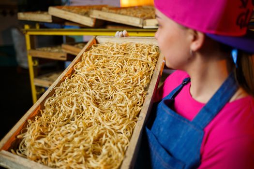 The girl works on the production of spaghetti. Making noodles. Pasta factory. Stage production of pasta. Raw noodles. Worker with a box of pasta.