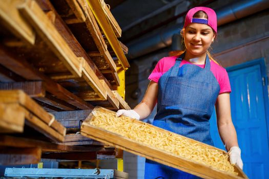 The girl works on the production of spaghetti. Making noodles. Pasta factory. Stage production of pasta. Raw noodles. Worker with a box of pasta.