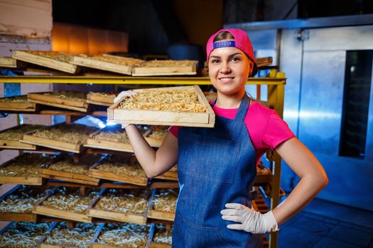The girl works on the production of spaghetti. Making noodles. Pasta factory. Stage production of pasta. Raw noodles. Worker with a box of pasta.