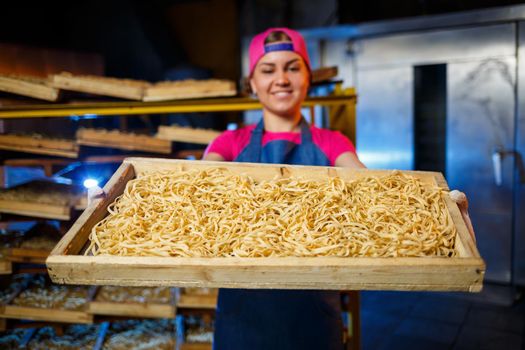The girl works on the production of spaghetti. Making noodles. Pasta factory. Stage production of pasta. Raw noodles. Worker with a box of pasta.