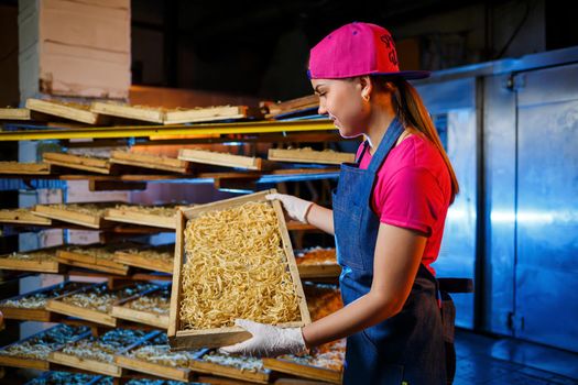 The girl works on the production of spaghetti. Making noodles. Pasta factory. Stage production of pasta. Raw noodles. Worker with a box of pasta.