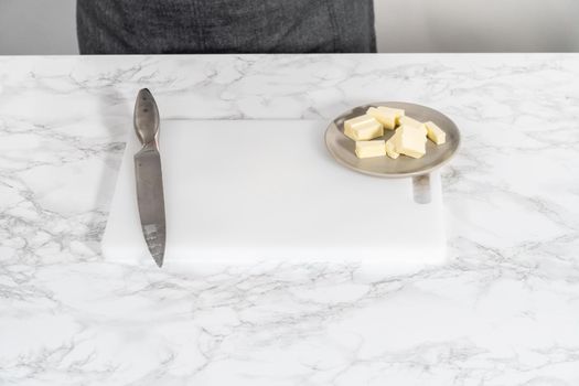 Slicing sticks of unsalted butter on a white cutting board.