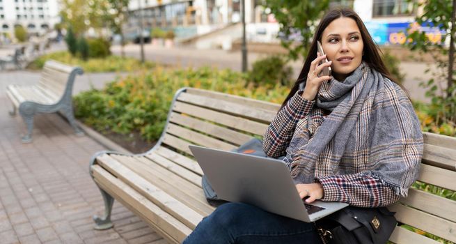 female freelancer working online on laptop while sitting in city on wooden benches.