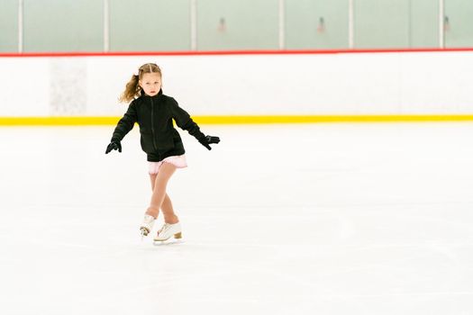 Little girl practicing figure skating on an indoor ice skating rink.