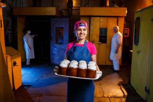 A baker girl holds a tray of hot pastries at the bakery. Production of bakery products. A tray of fresh crispy pastries.