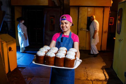 A baker girl holds a tray of hot pastries at the bakery. Production of bakery products. A tray of fresh crispy pastries.