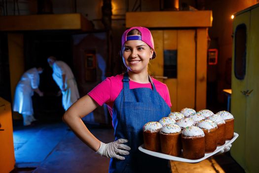 A baker girl holds a tray of hot pastries at the bakery. Production of bakery products. A tray of fresh crispy pastries.