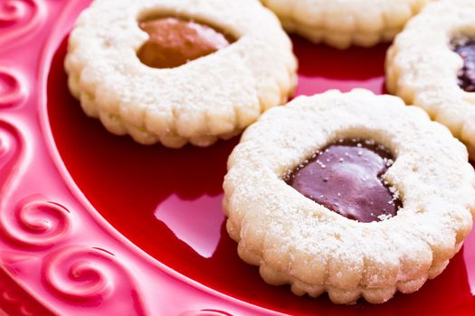 Linzer Torte cookies on red plate with powdered sugar sprinkled on top.