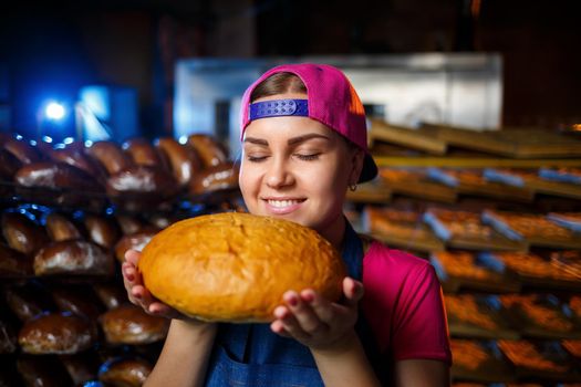 The stage of baking in a bakery. Portrait of a baker girl with bread in her hands against the background of shelving in a bakery. Hands of a baker with bread. Industrial bread production