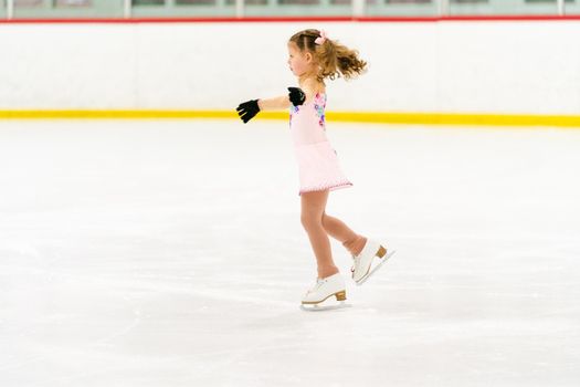 Little girl practicing figure skating on an indoor ice skating rink.