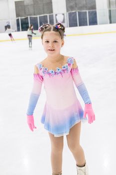 Little girl practicing figure skating on an indoor ice rink.