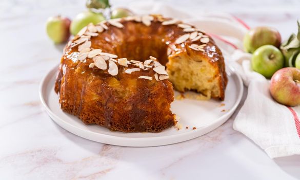 Slicing homemade apple bundt cake and garnishing with sliced almonds.