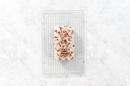 Flat lay. Glazing pumpkin bread with a white glaze and garnishing with shopped pecans.