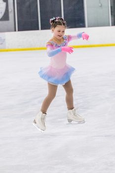 Little girl practicing figure skating on an indoor ice rink.