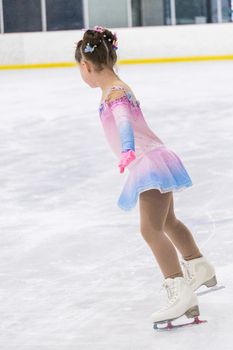 Little girl practicing figure skating on an indoor ice rink.