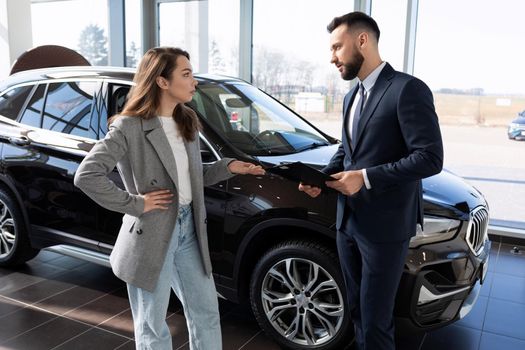 a young woman in a car dealership is interested in the details of the contract when buying a new car.