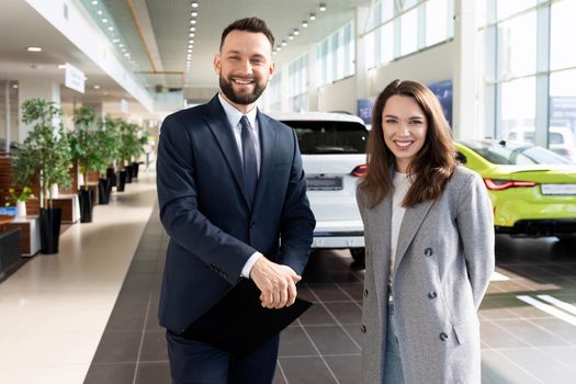 satisfied buyer and seller of a car dealership center on the background of new cars.