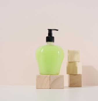 Transparent plastic bottle with green liquid on a wooden podium. Container for cosmetics