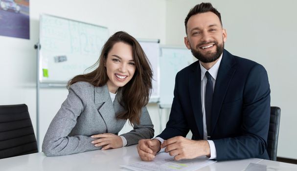man and woman employees of the company in presentable business clothes with a smile look at the camera while sitting at the table.