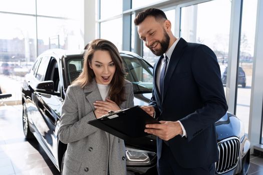 young woman versed in auto insurance pole together with consultant in car dealership.